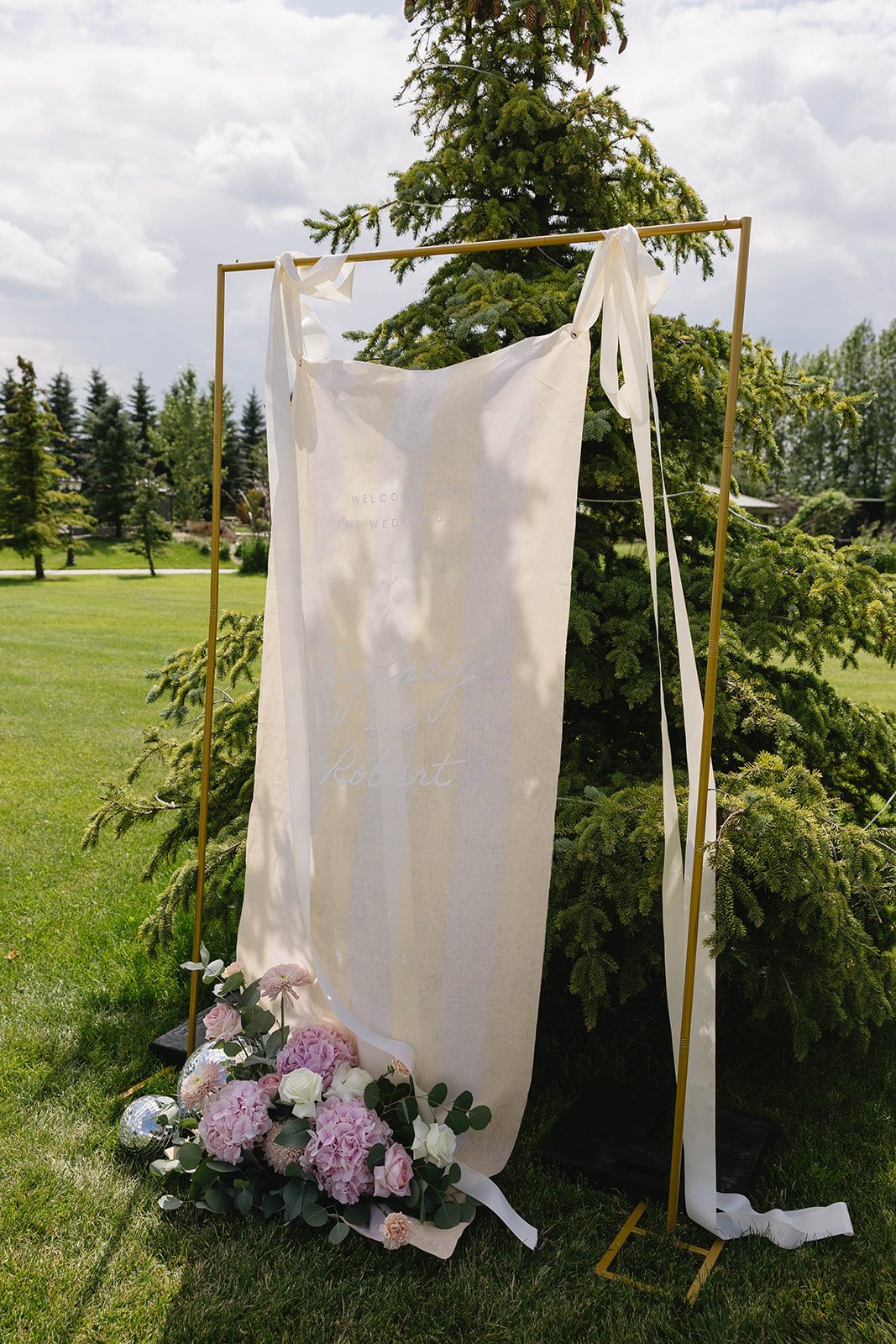 A welcome sign at Tangled Roots in Edmonton hanging from a gold frame with a low, pastel floral arrangement accenting the base.