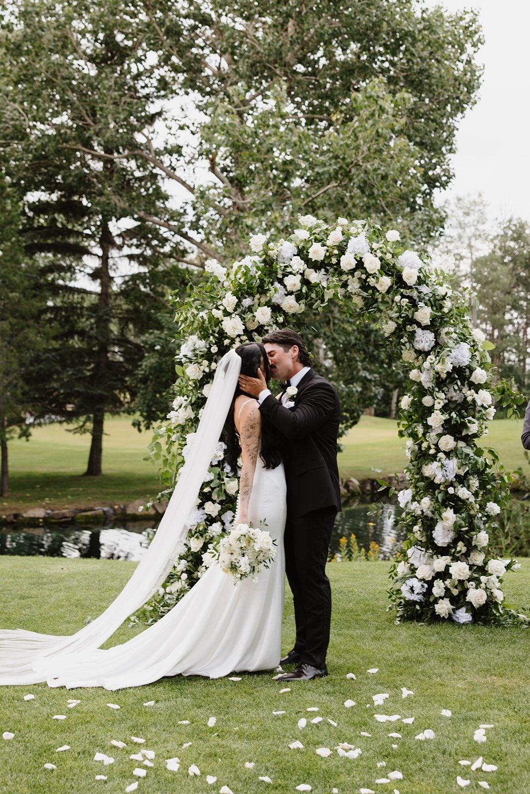 Cassidy + Adon Bride and groom share a kiss after saying "I do" in front of their lush green and white floral arch.
