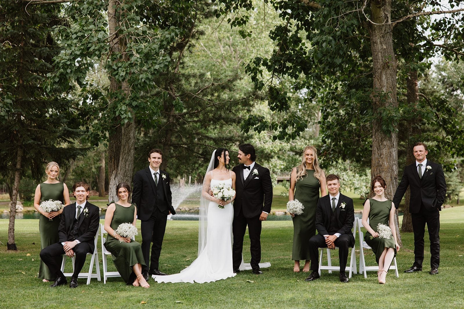 Cassidy + Adon Formal wedding party portraits in front of the pond at Hilltop with the bridesmaids in green dresses and baby's breath bouquets, men in black tuxedos with white boutonnières.