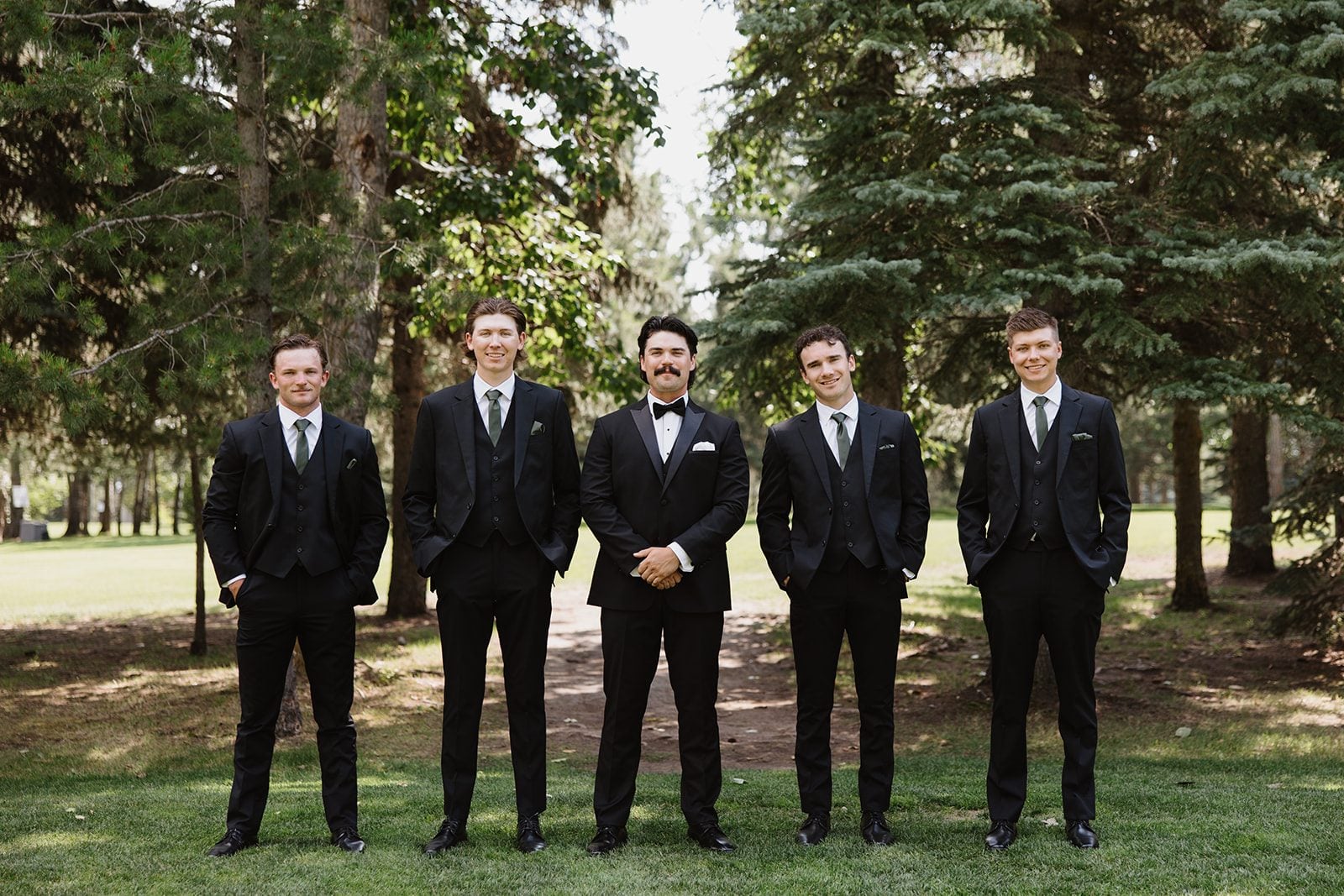 Cassidy + Adon Groom stands with his groomsmen in black suits and wearing white boutonnières for formal portraits at Hilltop.