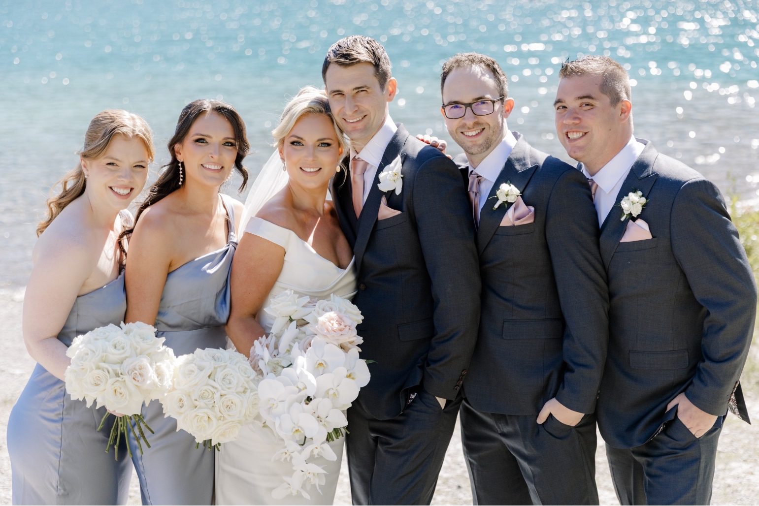 H&J Wedding Party Bride and groom standing with their wedding party against the mountain and lake backdrop at Lake Louise.