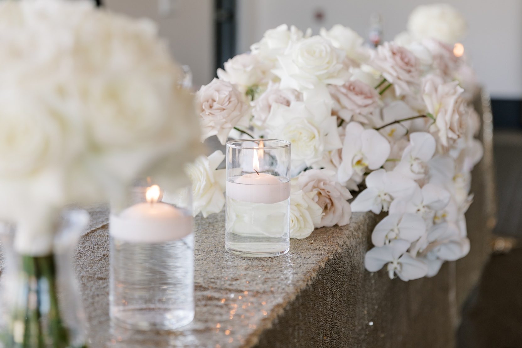 Head Table Flowers The bride's bouquet of ivory and blush roses with white orchids sitting on the glittering head table next to floating candles.