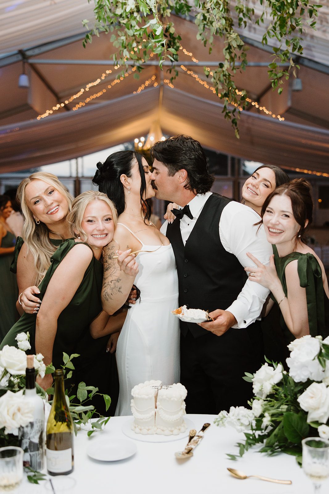 Cassidy + Adon Bride and Groom share a kiss after cutting the cake at their green and white reception t Hilltop Wedding Center.