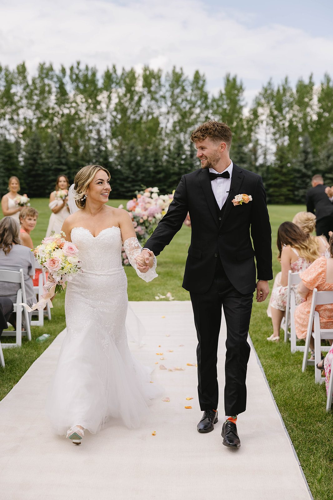 Couple holding hands and smiling at each other as they exit the aisle of their modern, pastel garden wedding at Tangled Roots.