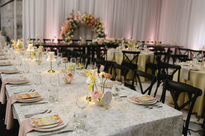 Looking down the long rectangular table with the head table the background, pastel ikebana inspired centrepieces run down the centre of the table on softly patterned ivory table linens.