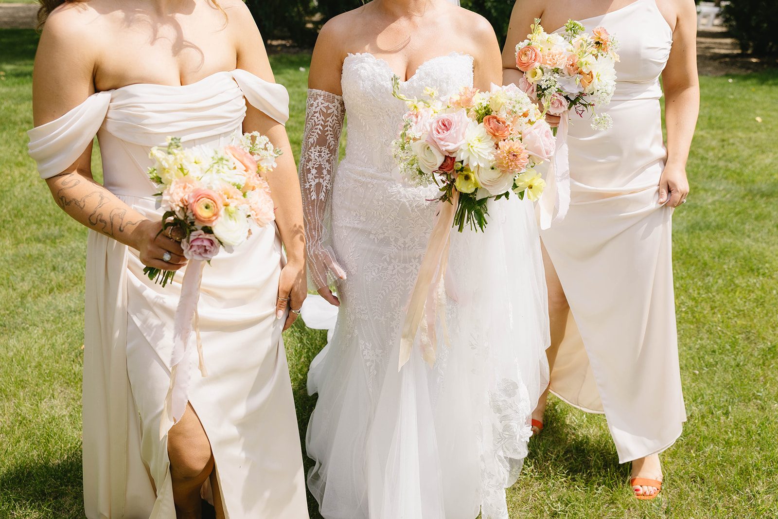 Bride and her bridesmaids in a modern pastel garden wedding holding their bouquets of dahlias, garden roses, stock, lisianthus, ranunculus and orlaya with trailing silk ribbons.