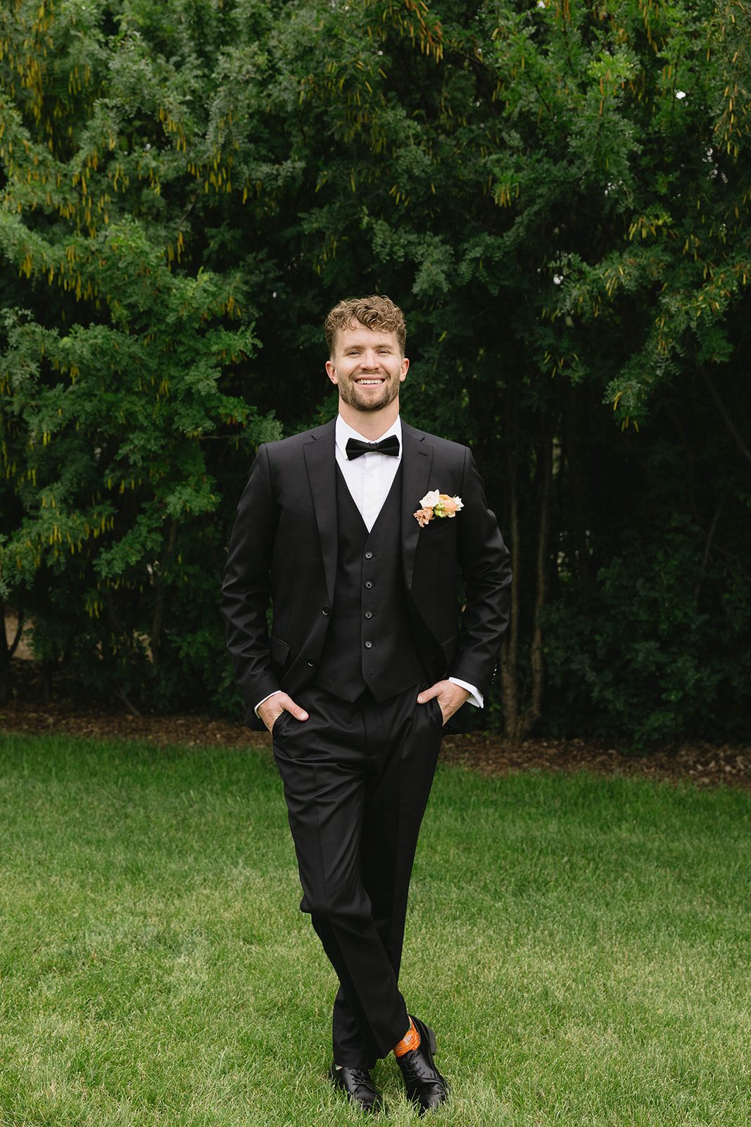 Groom wears a black tuxedo and a pastel pocket square styled boutonnière of lisianthus, ranunculus and spray roses.