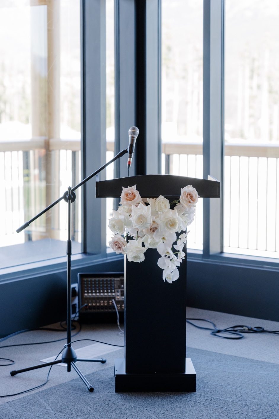Podium Arrangement Black podium decorated with cascading white orchids, and roses set against tall windows overlooking mountain scenery.