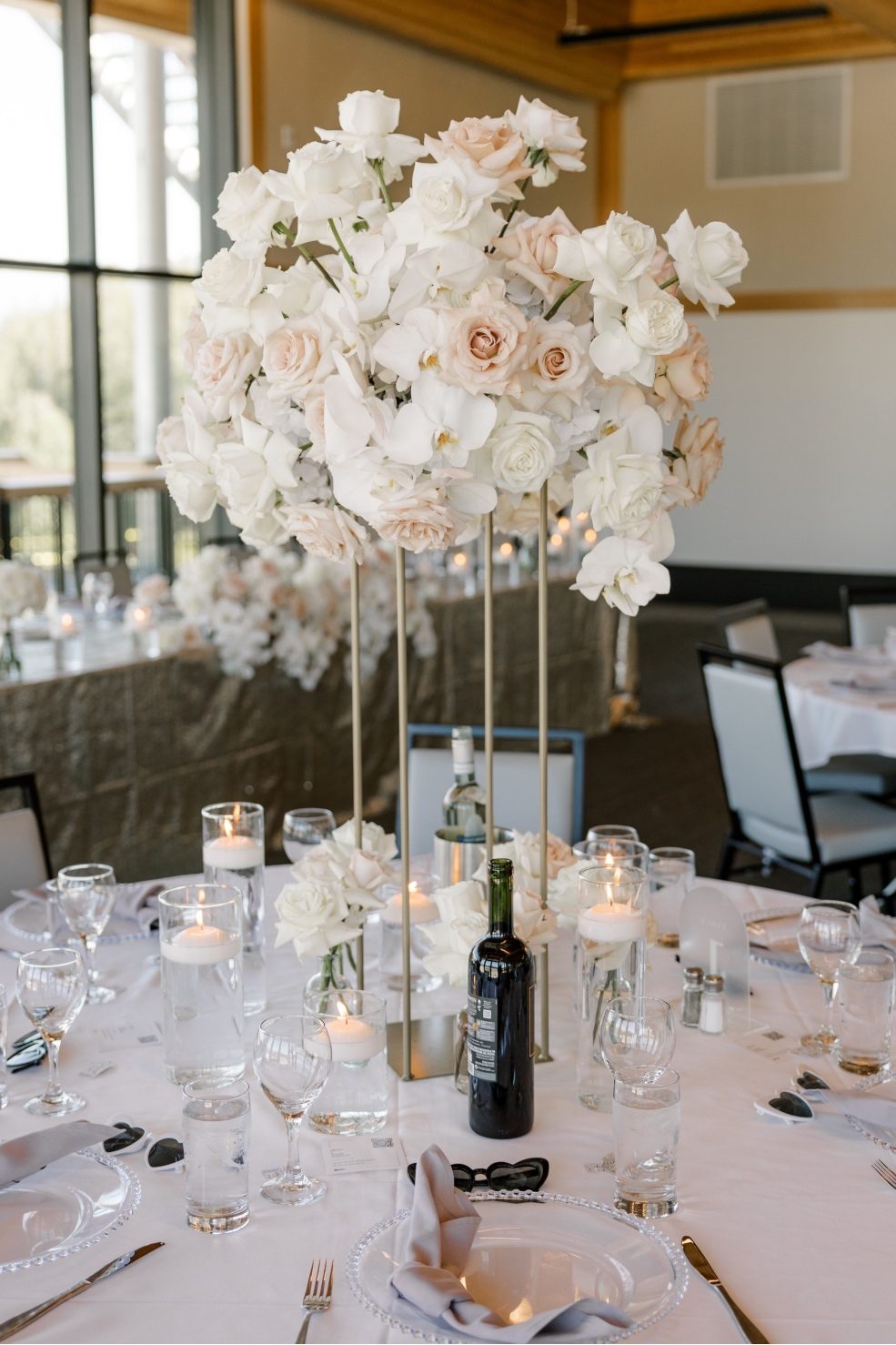 Stunning Centrepiece Tall reception centrepiece of white and blush roses and orchids on top gold stands, surrounded by elegant tile settings with candles and glassware.