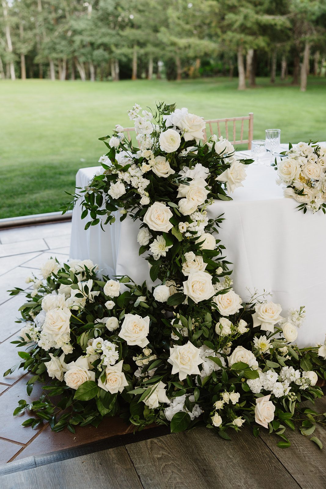 Cassidy + Adon Close up of the green and white floral arrangements decorating the sweetheart table including roses, dahlias, ranunculus and eucalyptus.