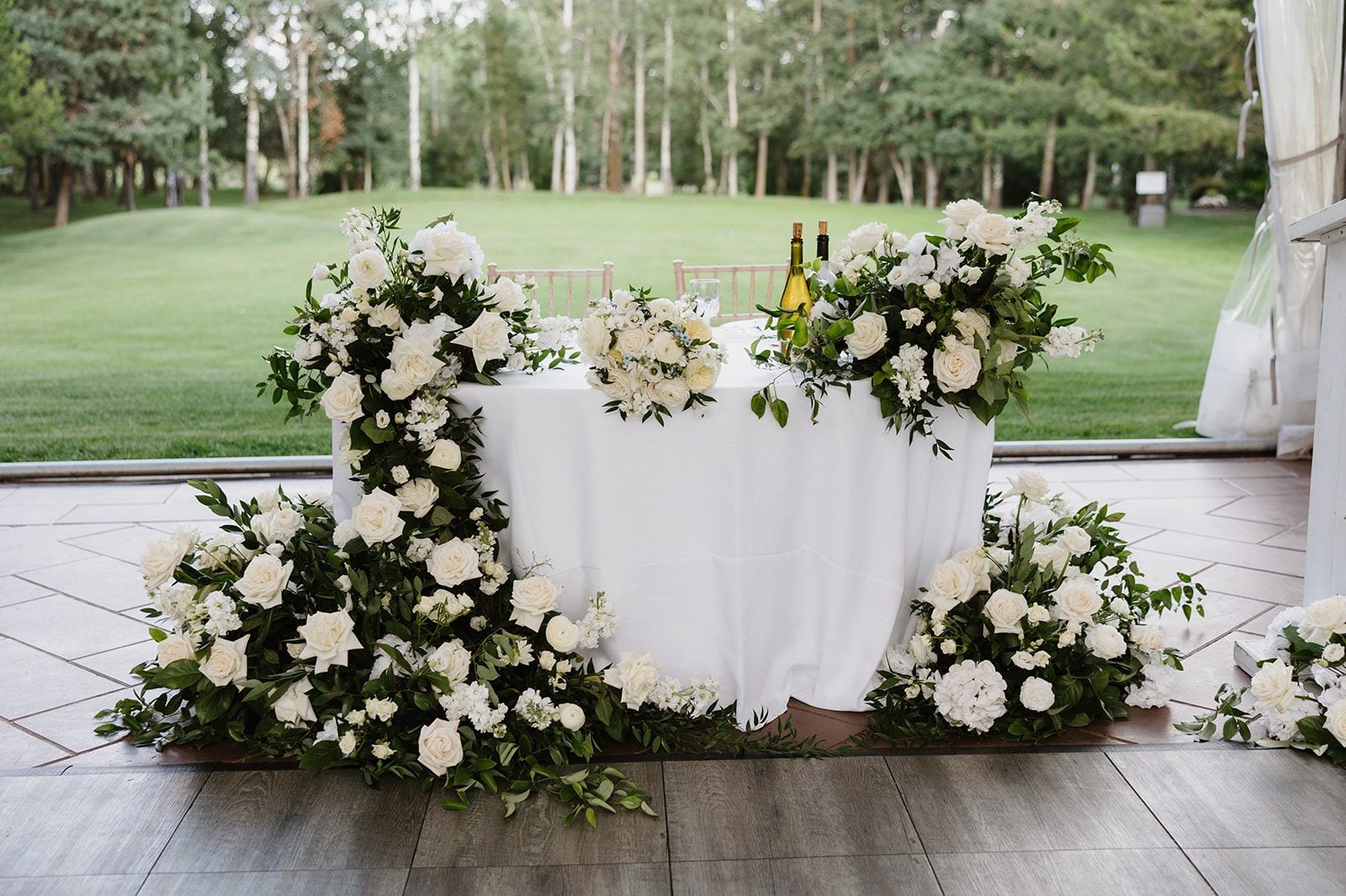 Cassidy + Adon Green and white sweetheart table decorated with floral arrangements featuring dahlias, roses, ranunculus, lisianthus and eucalyptus.