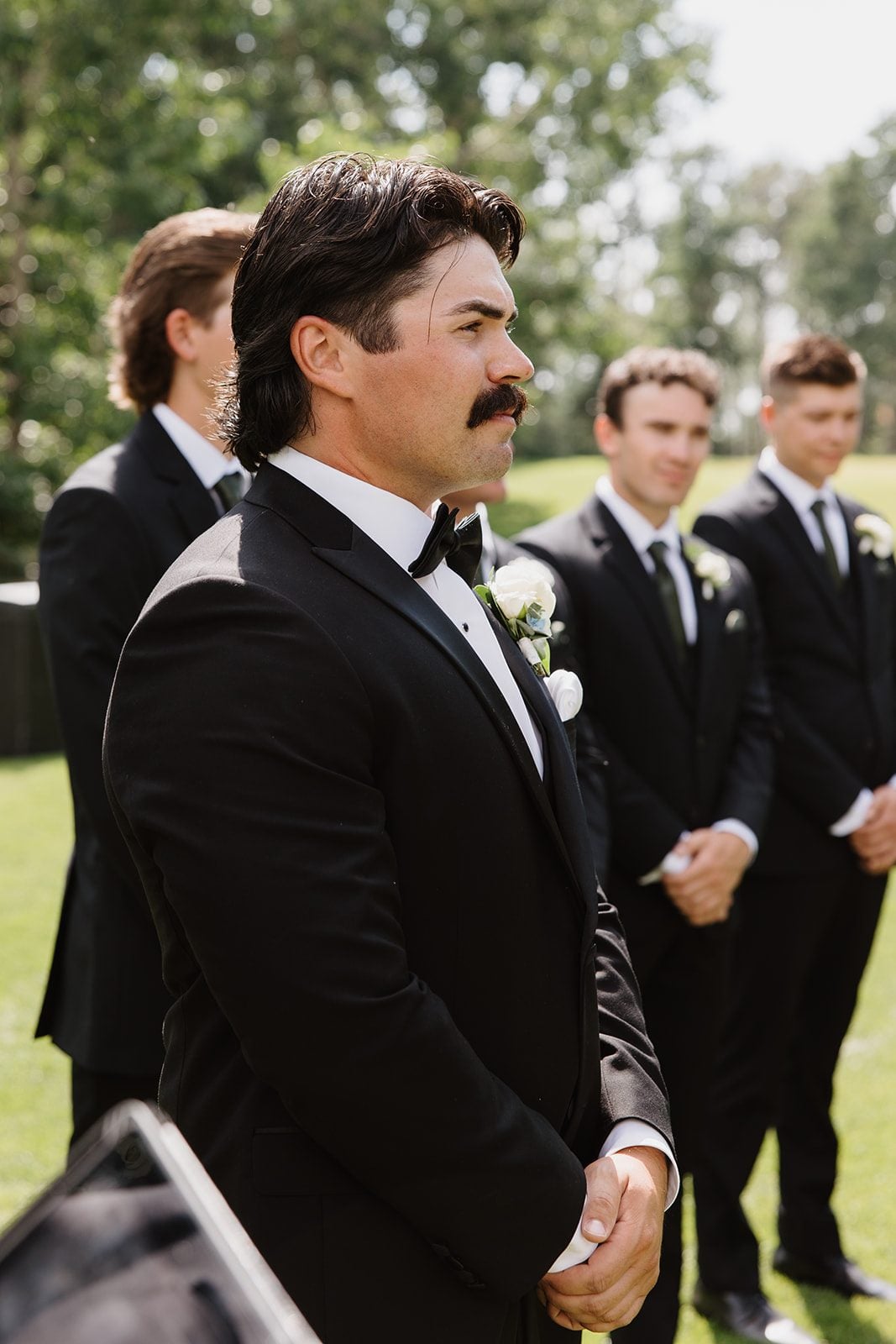 Cassidy + Adon The groom awaiting his bride at the alter of this green and white Hilltop wedding, wearing a white spray rose and ranunculus boutonnière.