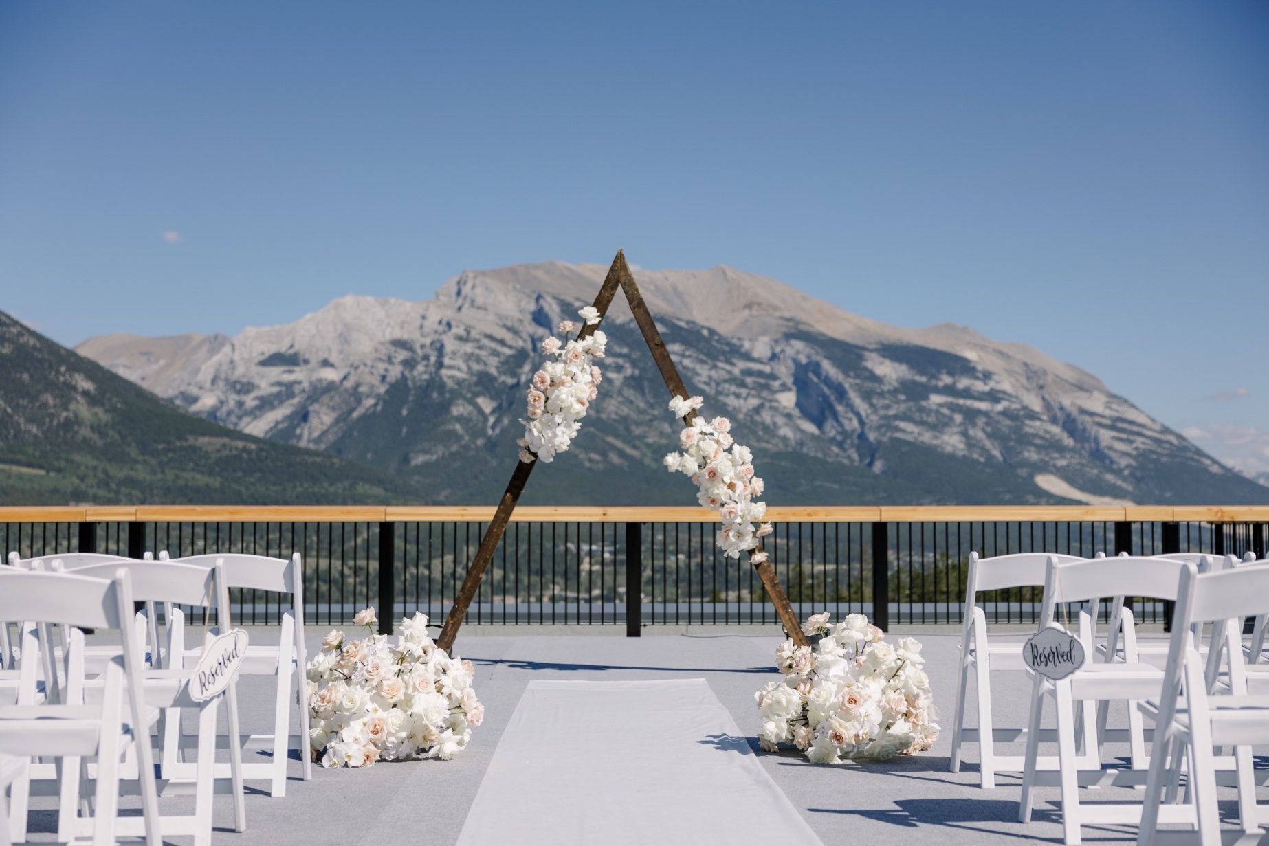 Wedding Altar Triangular wooden ceremony arch adorned with cascading white and blush roses and orchids, set against Lake Louise's panoramic mountain view.