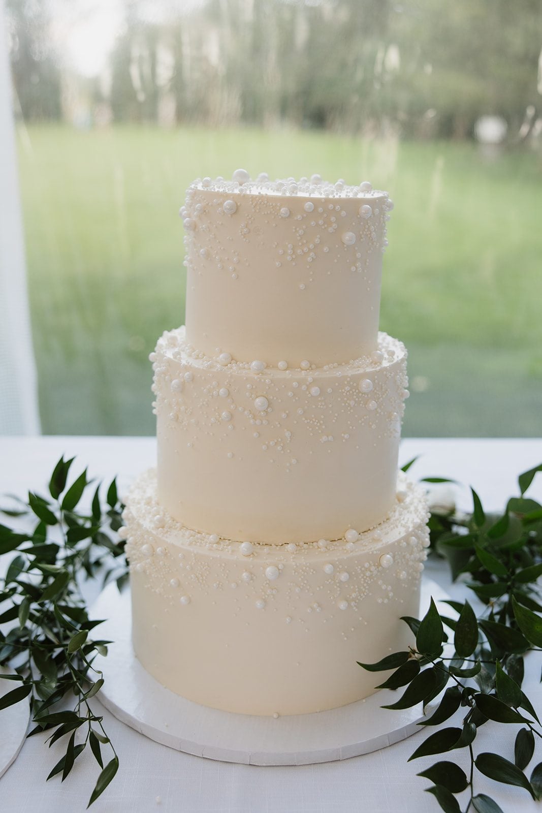 Cassidy + Adon Traditional three tier ivory wedding cake with loose stems of Italian ruscus to compliment their green and white wedding palette.