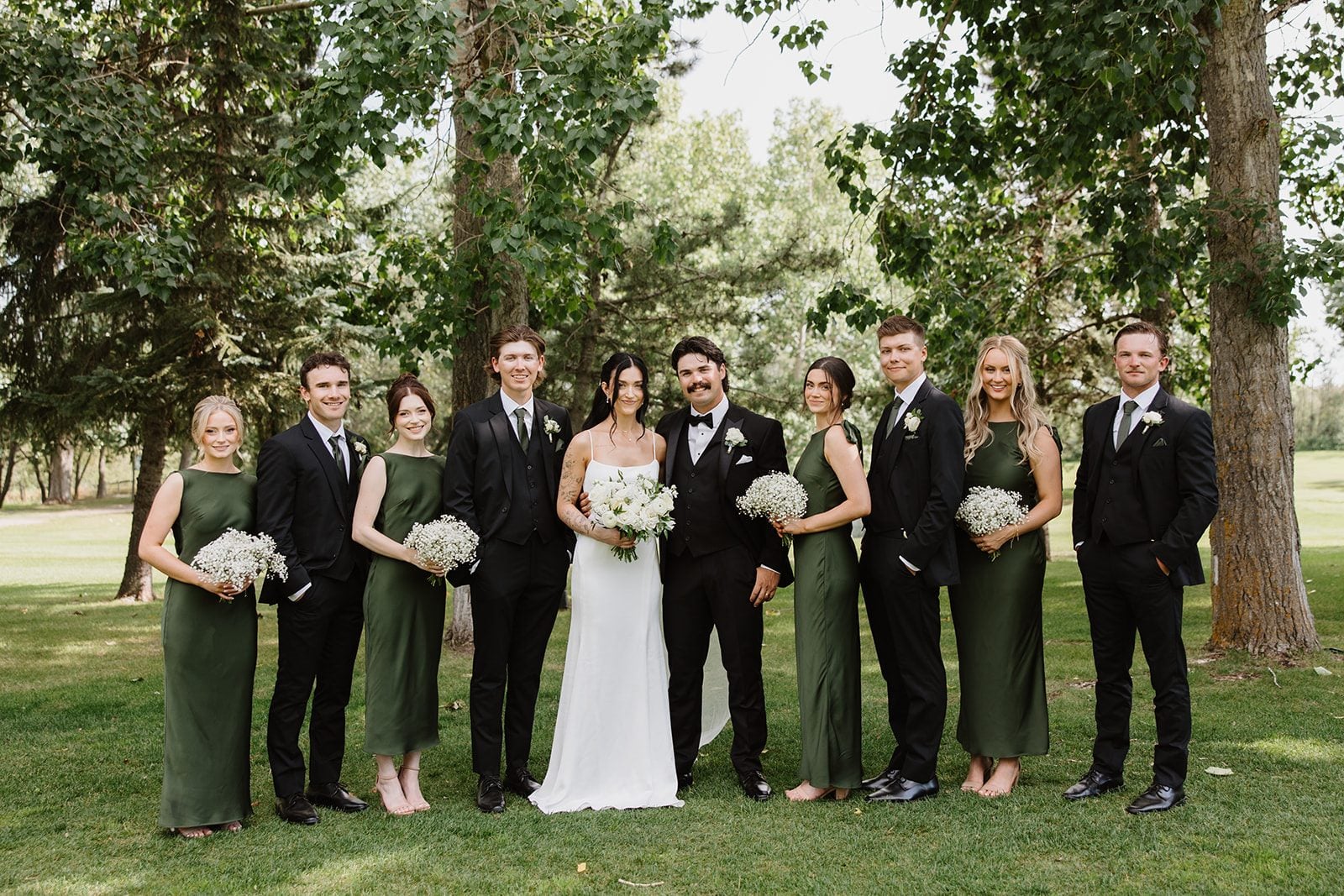 Cassidy + Adon Formal wedding party portraits of this green and white wedding on Hilltops grounds. Bridesmaids in green dresses and holding baby's breath bouquets, Bride with an all white bouquet. Groom and groomsmen wearing black suits with white boutonnieres.