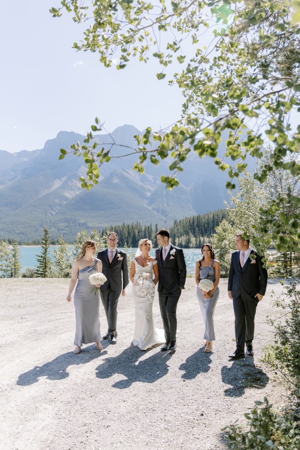 Wedding Party Wedding Party walking together along the lakeshore framed by overhanging leaves and mountain views.