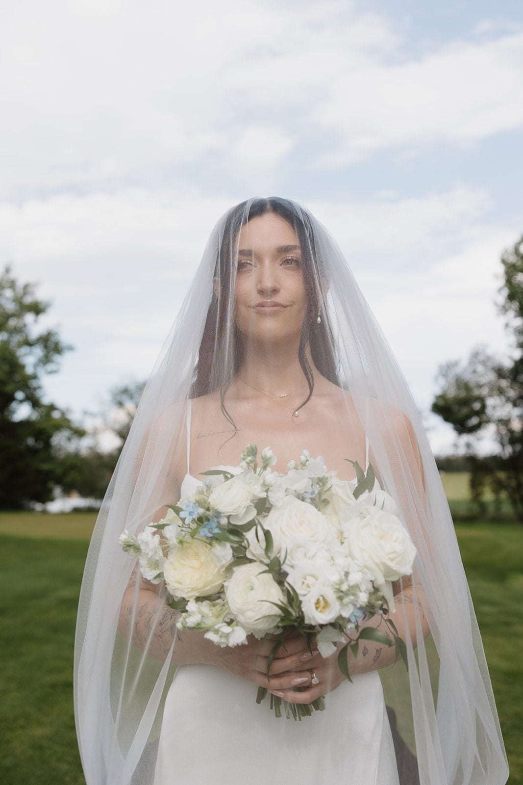 Cassidy + Adon Traditional portrait of our Calyx Bride holding her white bouquet of roses, ranunculus, sweet peas and eucalyptus, with her veil covering both her and her bouquet.