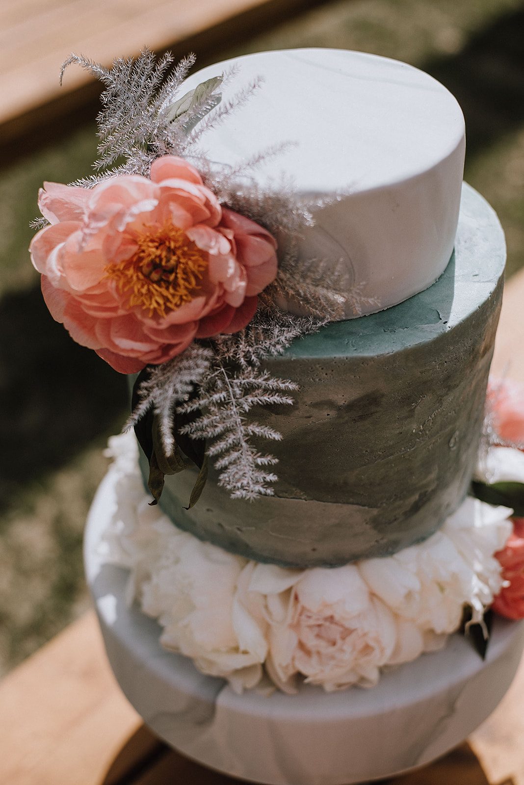 A coral charm peony with plumosa fern on a wedding cake.