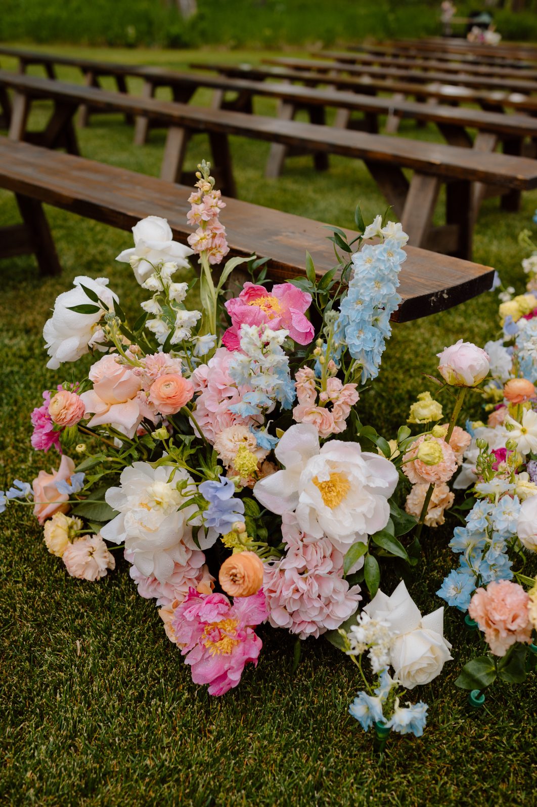 White and coral peonies mixed among other pastel toned spring flowers in a beautiful aisle arrangement at a wedding.