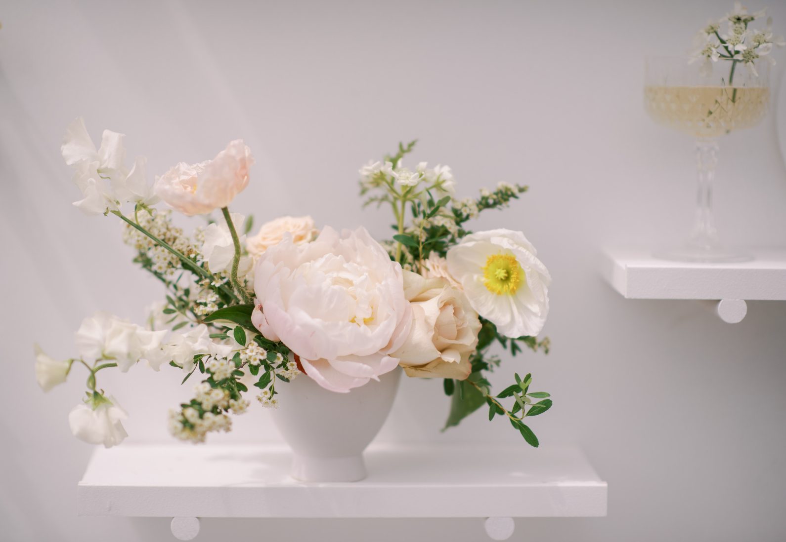 A white peony with other white spring blooms in a ceramic container.
