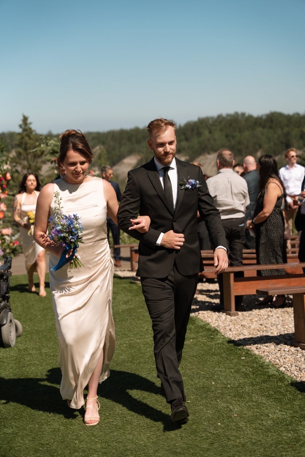 Blue Bridesmaid A bridesmaid in her champagne dress carrying a blue bouquet exiting the ceremony on the arm of a groomsmen wearing a blue boutonnière.