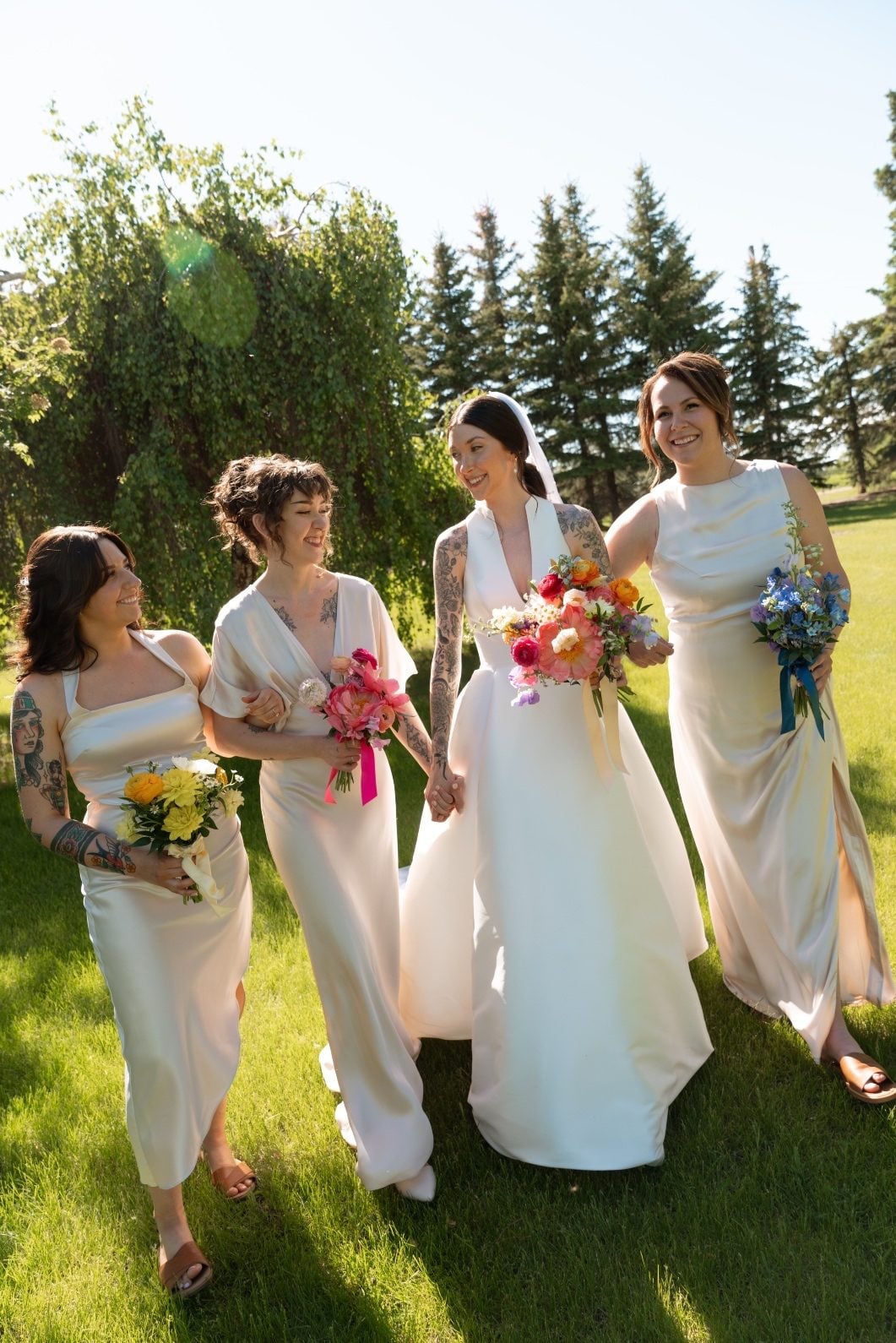 Colourful Bridal Party at River’s Edge The bride and her bridesmaids walking in the sunshine holding their colourful bouquets.