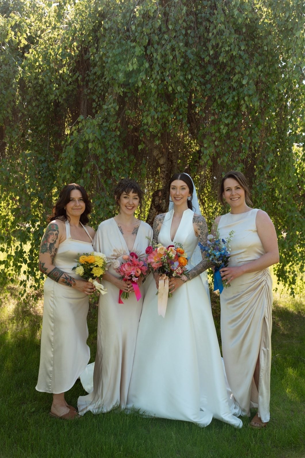 Colourful Bridal Party The bride and her brides maids stand under a tree with their pale gowns, holding vibrant, colourful bouquets.