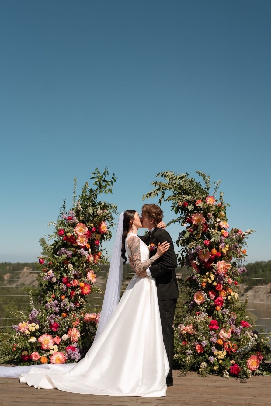 Colourful Broken Arch at River’s Edge The bride and groom share a kiss to make it official in front of their beautiful, colourful broken arch.