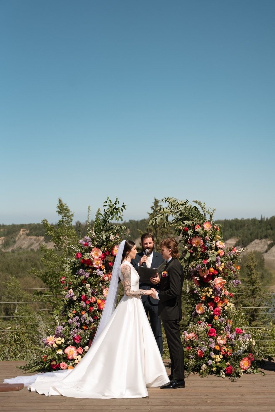 Colourful Broken Arch The bride and groom during the ceremony with their hands clasped together in front of the stunning, colourful broken arch.