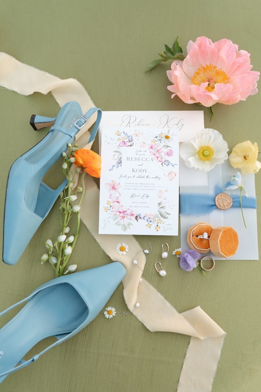 Colourful Flatlay with Flowers A flat lay image showing the brides blue shoes, invitation, rings with colourful peonies, poppies, sweet peas and chamomile.