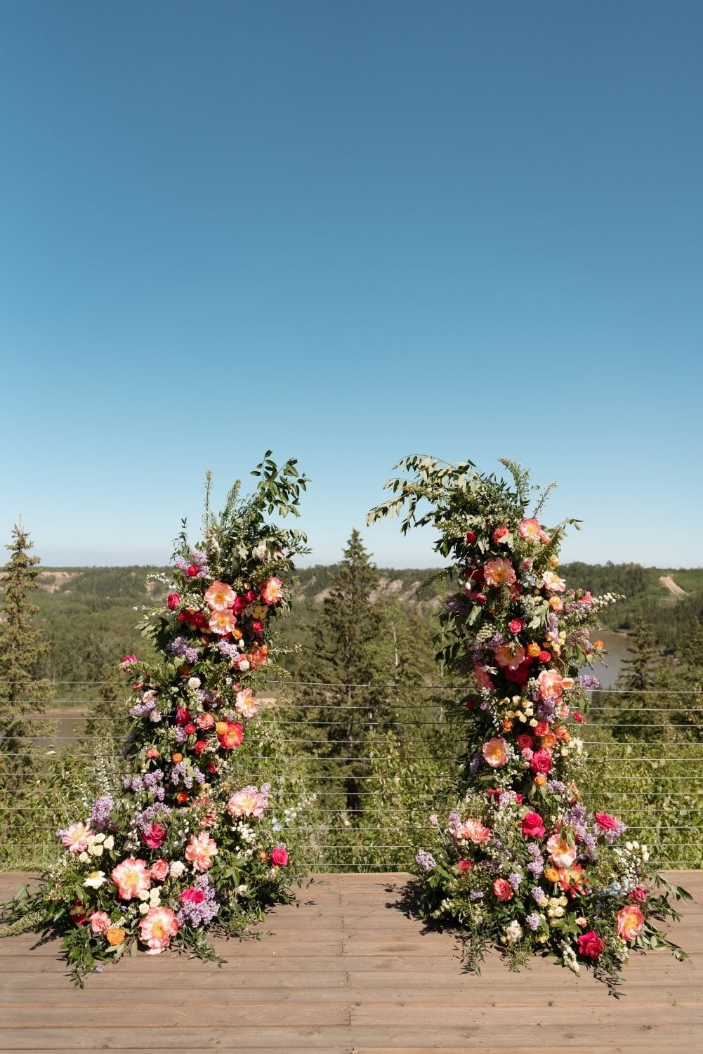 Colourful Garden Inspired Broken Arch A striking, colourful broken arch full of garden inspired blooms, with the scenic views of River's Edge behind it.