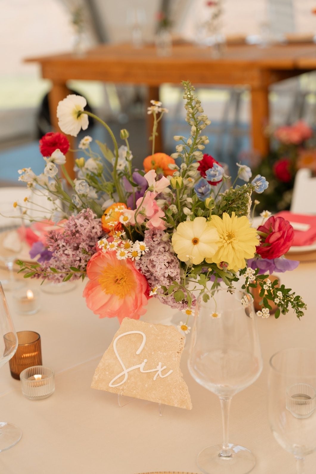 Colourful Garden Inspired Centrepiece An abundant, colourful, gardeny centrepiece on the round guest tables featuring peonies, ranunculus, poppies, lilacs, flowering spirea, ranunculus and chamomile.