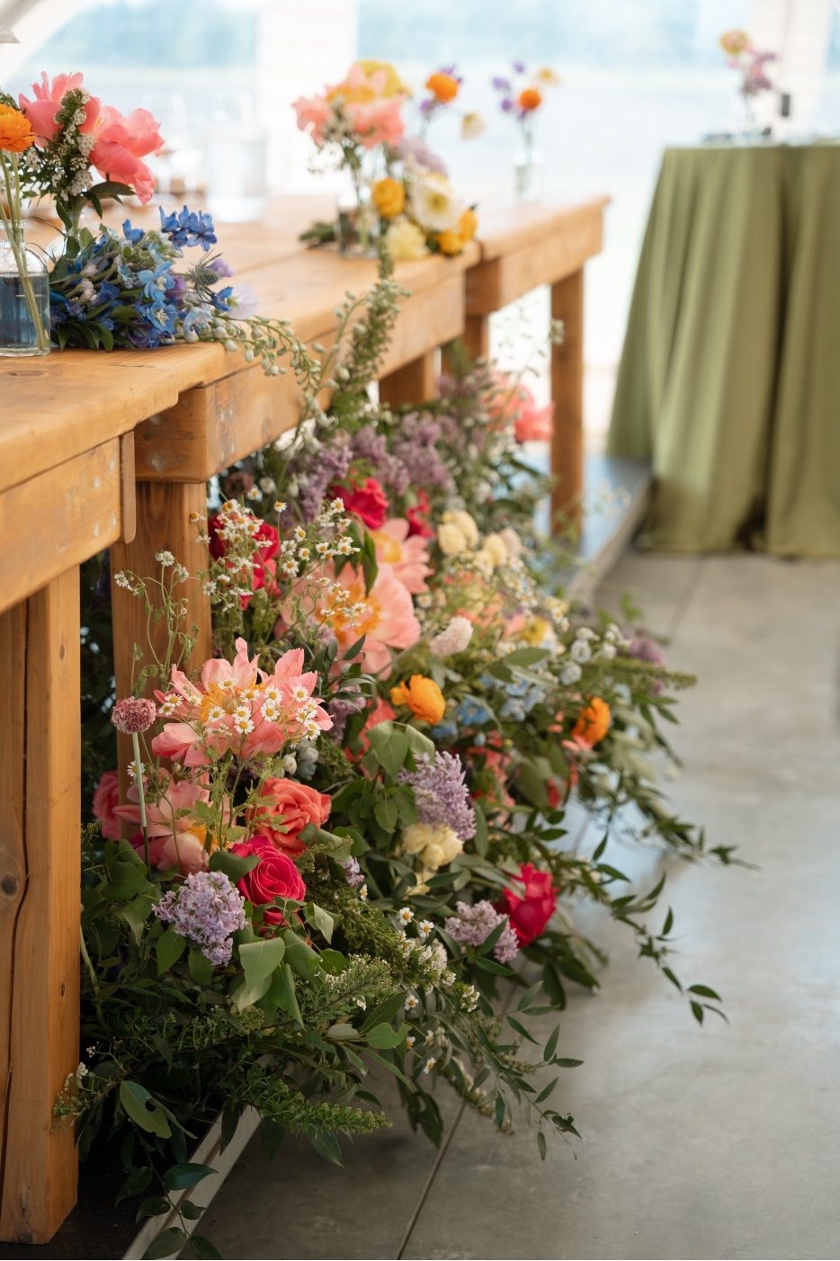 Colourful Reception Flowers In front of the head table, a lush, colourful arrangement of gardeny blooms including peonies, ranunculus, delphinium, flowering spirea, roses, scabies and chamomile.