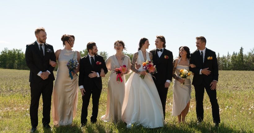 Colourful Wedding Feature A bride and groom with their wedding party wearing neutral attire and carrying colourful florals walking through the fields at River's Edge.