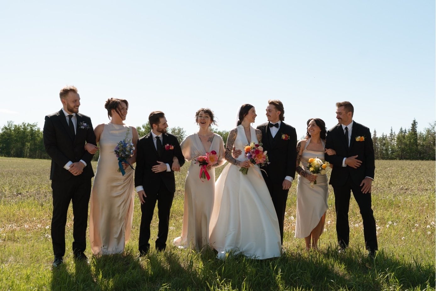 Colourful Wedding Party at River’s Edge The bride and groom walking with their wedding party through the field at River's Edge.