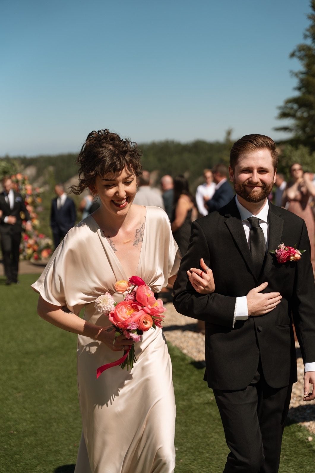 Coral Bridesmaid A bridesmaid in her champagne dress carrying a pink bouquet exiting the ceremony on the arm of a groomsmen wearing a pink boutonnière.