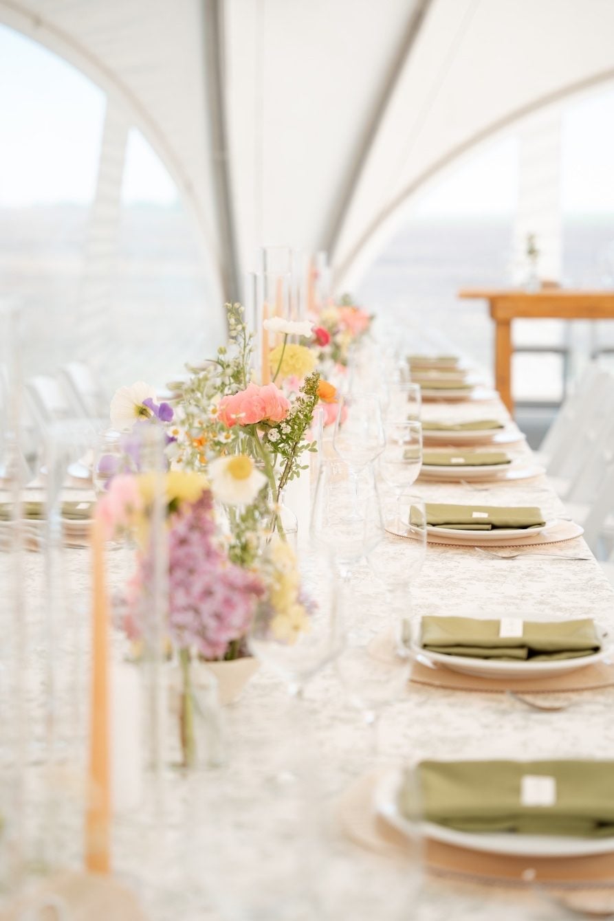 Garden Inspired Centrepieces Looking down the length of the harvest guest tables. Neat line of plates with folded green napkins on top, and ikebana centrepieces with taper candles down the center of the table.