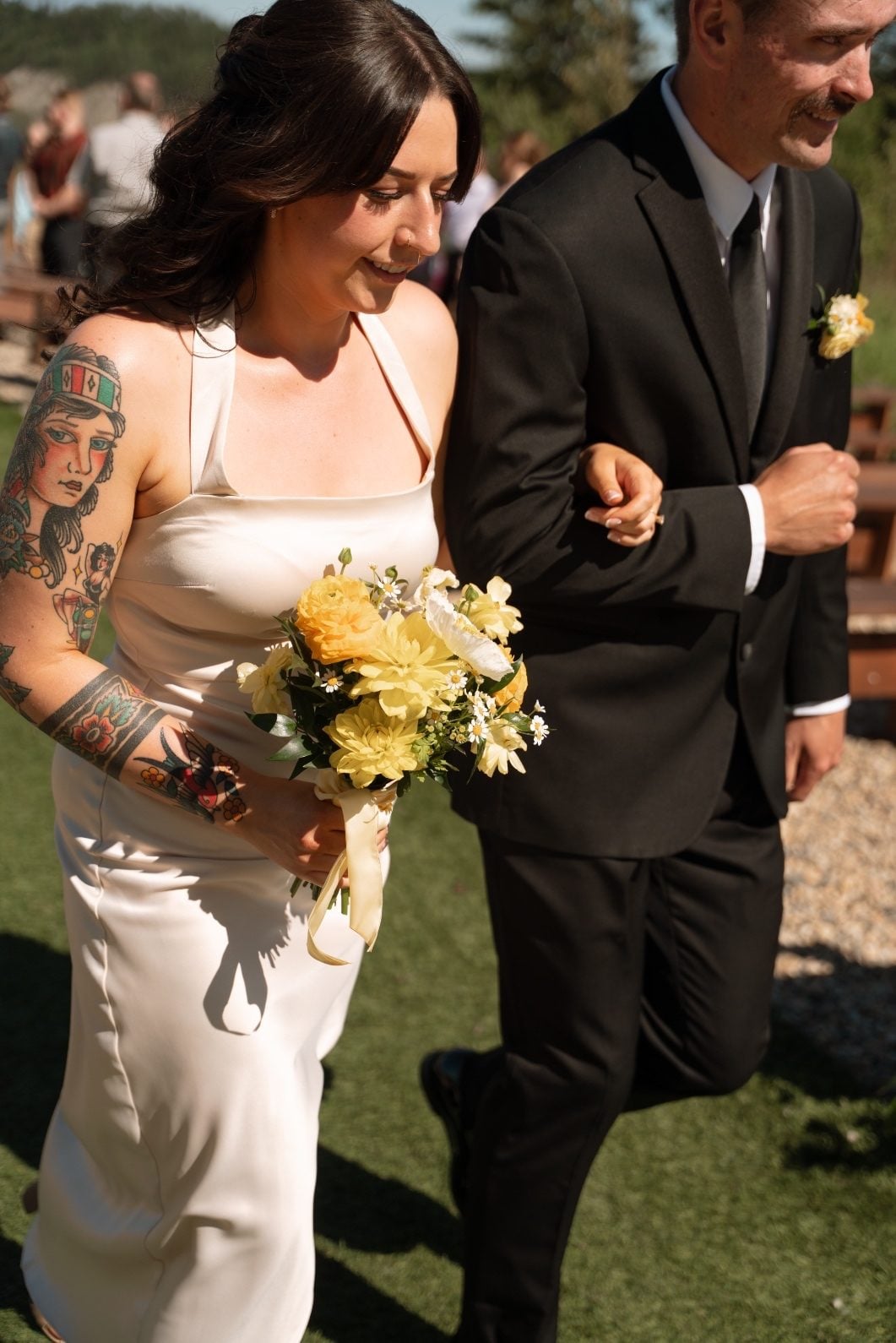 Yellow Bridesmaid A bridesmaid in her champagne dress carrying a yellow bouquet exiting the ceremony on the arm of a groomsmen wearing a yellow boutonnière.