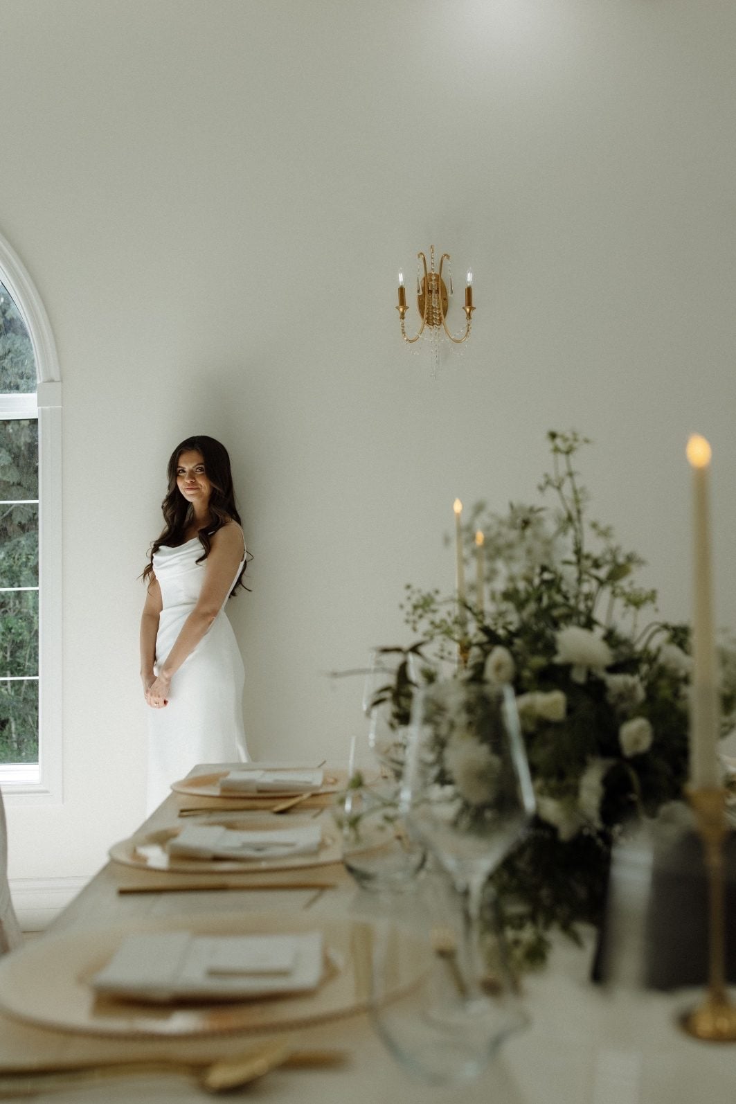 Bride at White + Green Reception at Archway Manor Bride leans against the wall behind a guest table for their white and green wedding at Archway Manor.