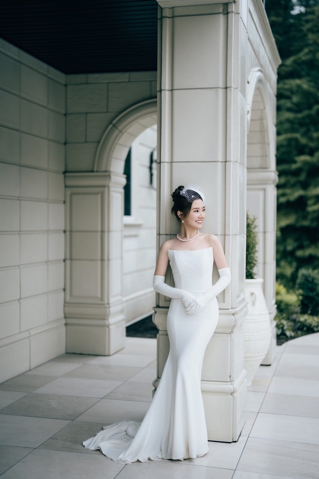 Bride stands against a column wearing a sleek white reception gown at this luxurious Archway Manor Wedding.