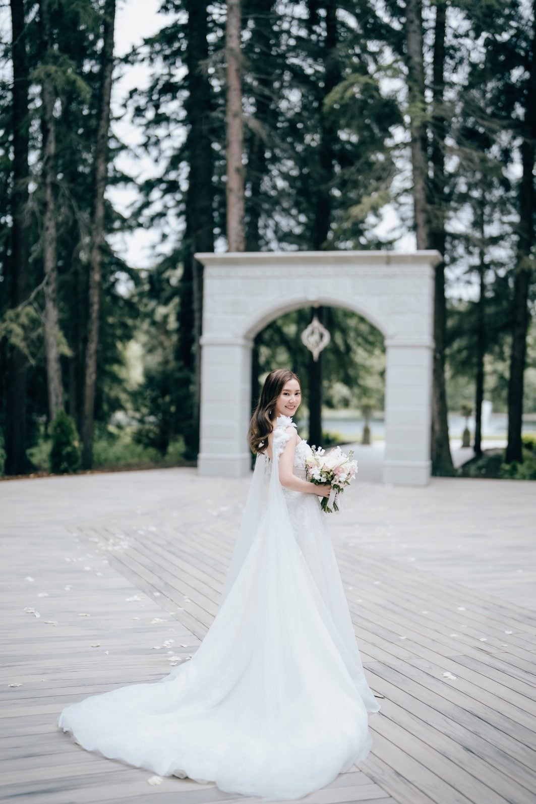Bride smiling softly holding her pale bouquet outside at Archway Manor.