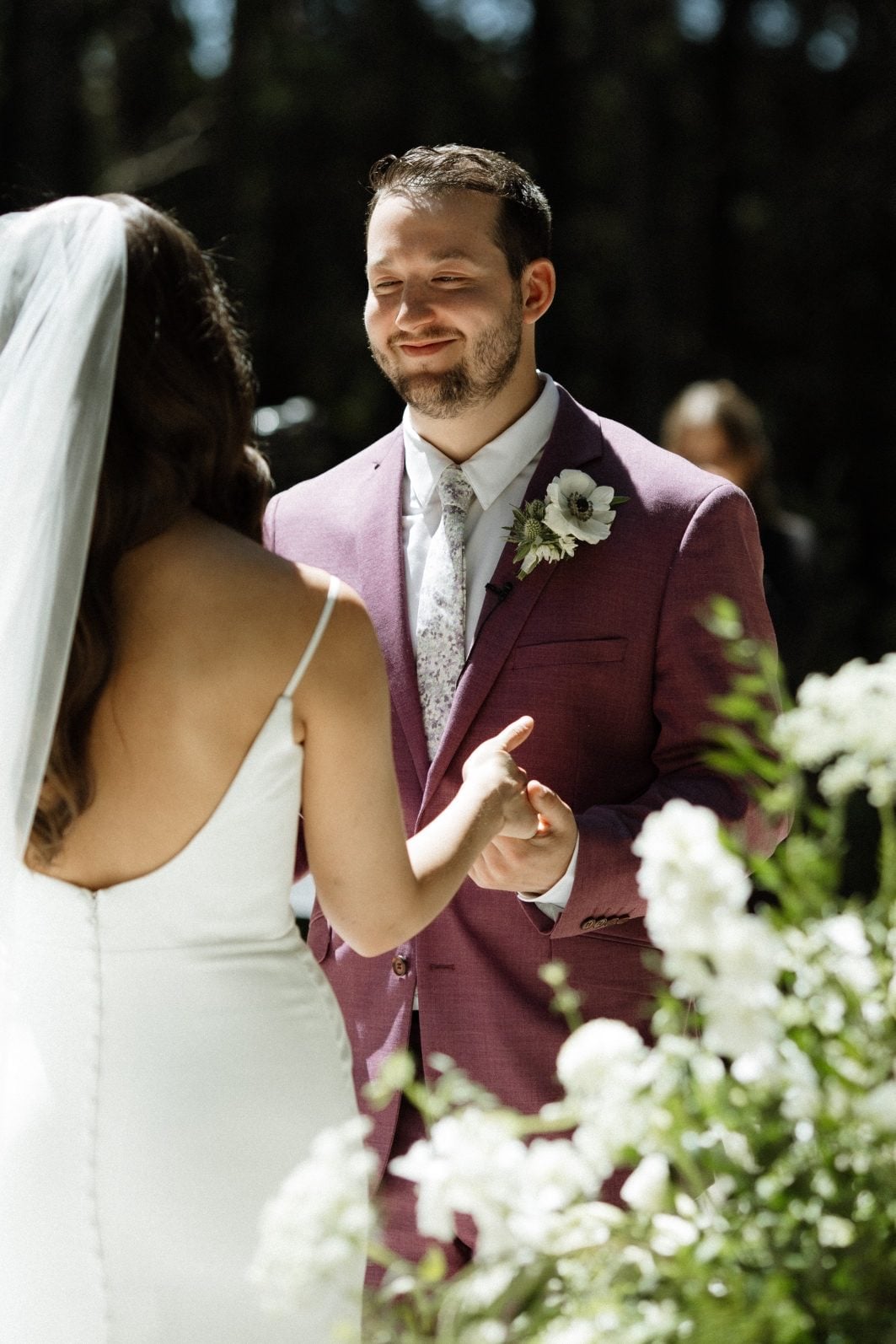 Groom with White Anemone Boutonniere Bride looks at the groom during white and green ceremony at Archway Manor.