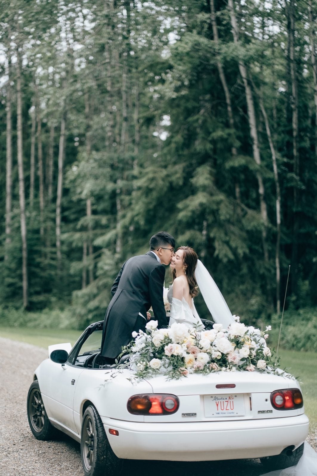 Bride and groom share a kiss in their white convertible getaway car adorned with flowers.