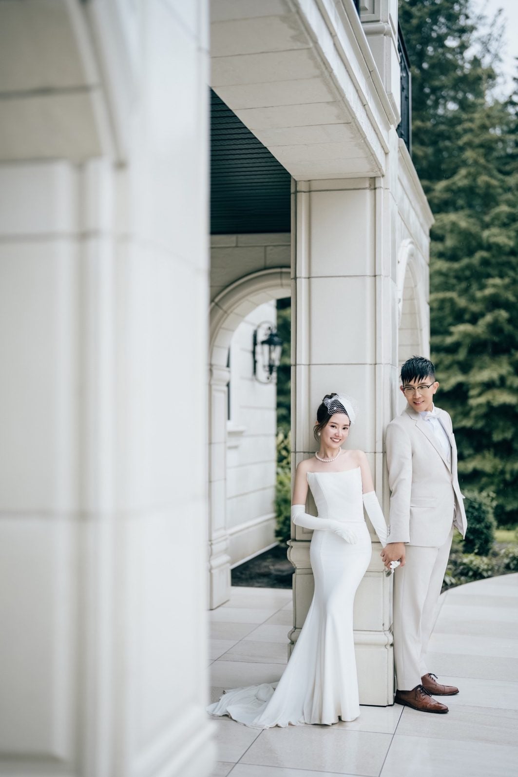 Bride wearing her reception gown poses with Groom outside Archway Manor.