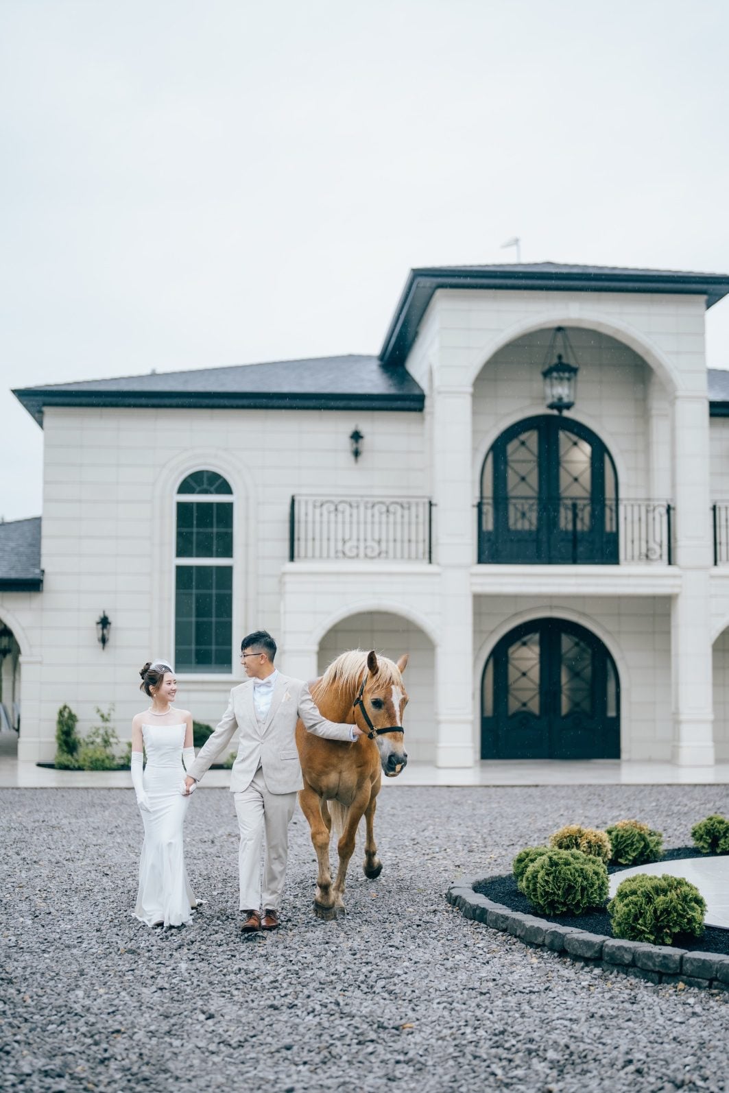 Like out of a fairy tale, the bride and groom walk the grounds of Archway Manor with a brown horse.