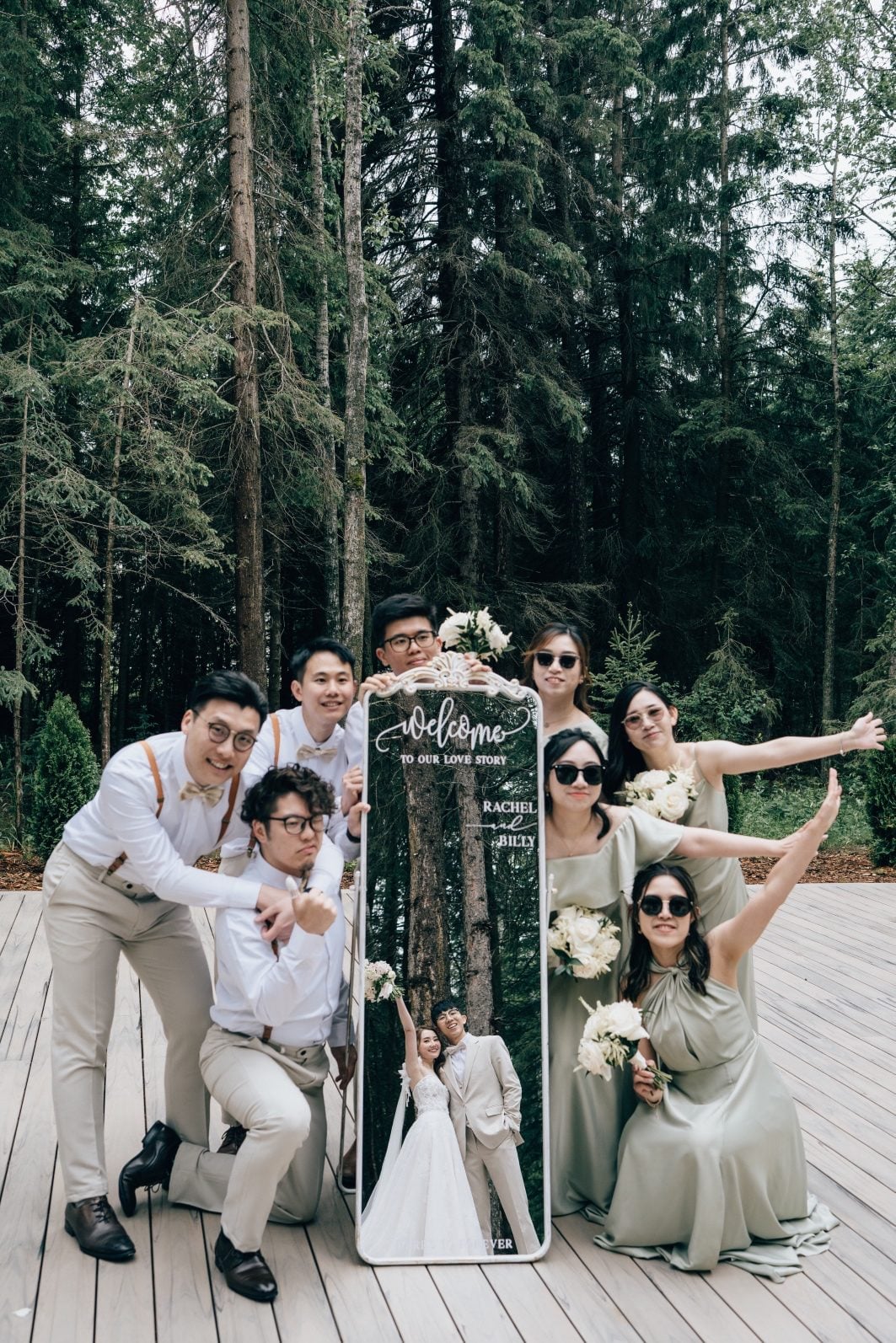 Wedding party strike a silly pose around a mirror showing Bride and Groom in the reflection.