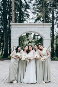Bride smiling demurely with her beautiful bridesmaids in sage gowns.