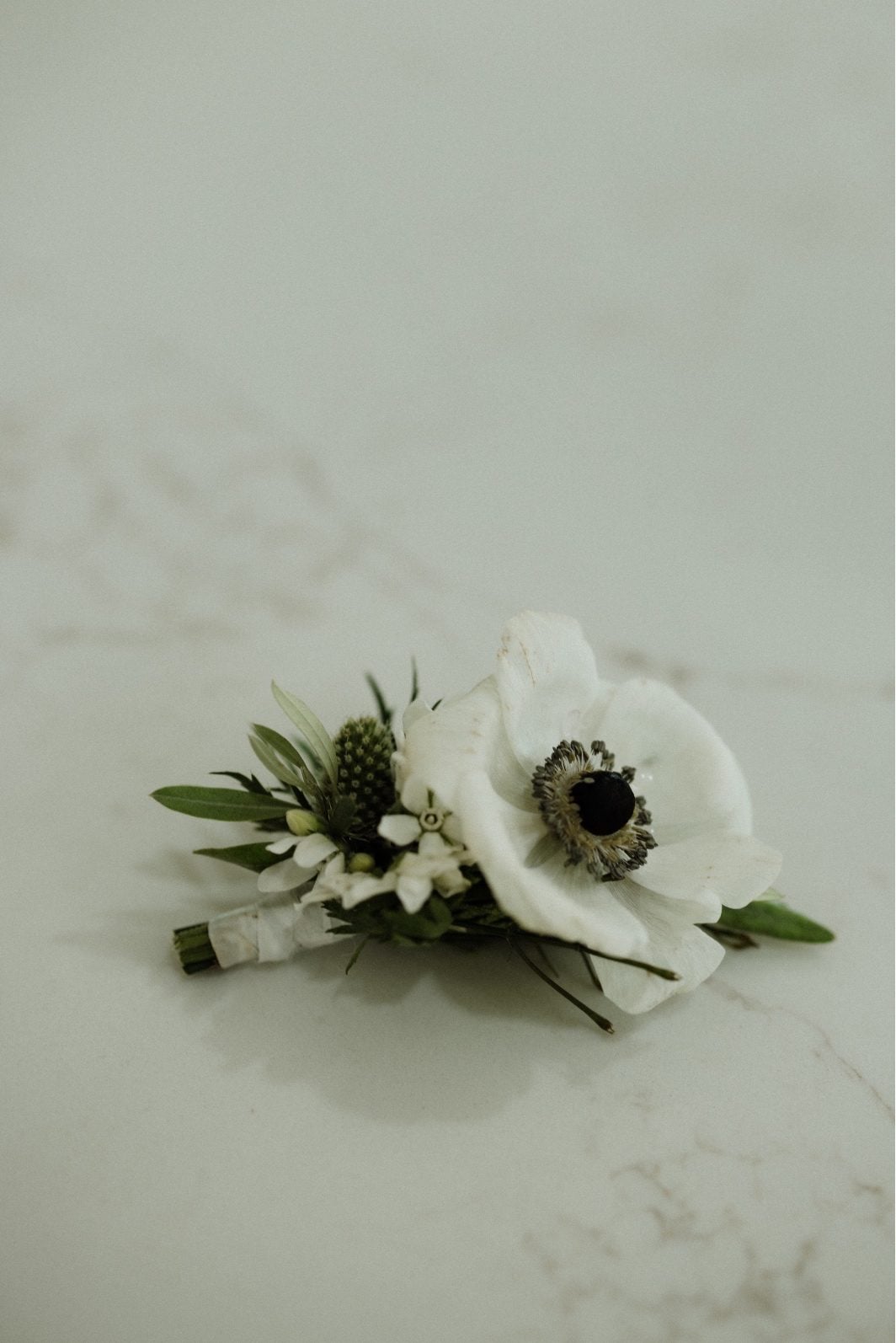 White Anemone Handsome boutonnière for the groom at a white and green wedding featuring a white anemone with dark centre.