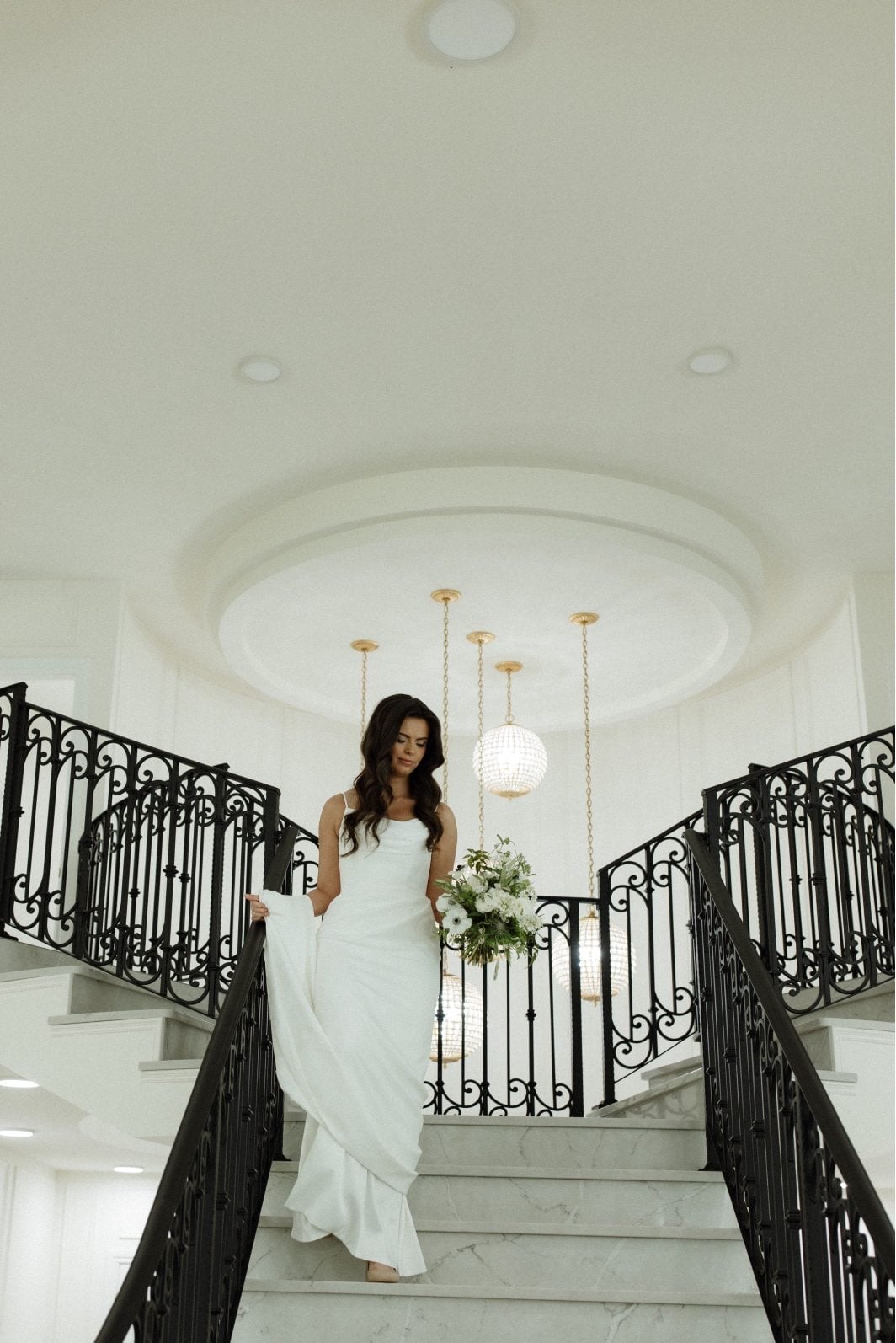 White and Green Bride at Archway Bride holding her white and green bouquet of anemone, orlaya, ranunculus, scabiosa, ranunculus and lisianthus while coming down the grand staircase at Archway Manor.
