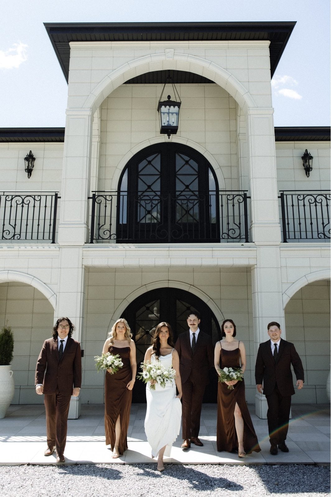 White and Green Wedding with Chocolate Bridal Party Calyx bride with her bridal party in chocolate attire, stand outside Archway Manor smiling.